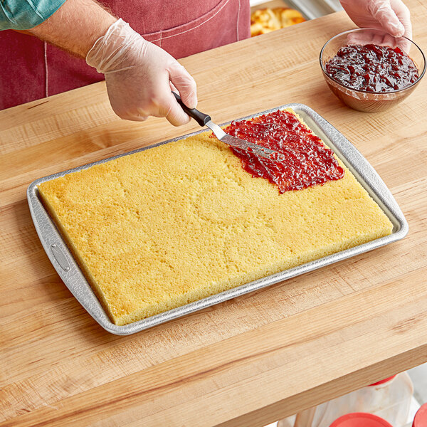 A person spreading jam on a cake using a DoughMakers aluminum pebbled jelly roll pan.