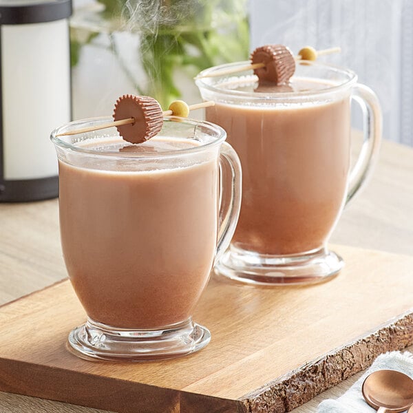 A glass mug of REESE'S hot chocolate with a spoon and marshmallows on top.