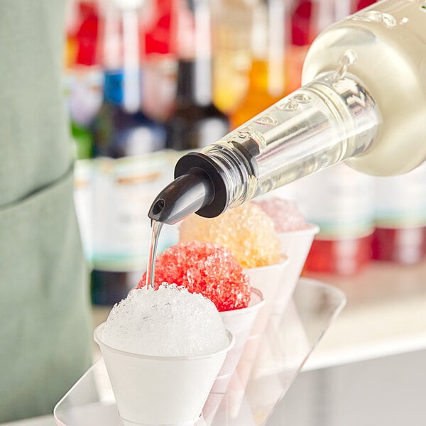 A person pouring Hawaiian Shaved Ice Pina Colada Snow Cone Syrup into small cups of snow.