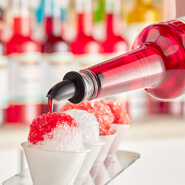A person pouring Hawaiian Shaved Ice Watermelon snow cone syrup into a white cup.