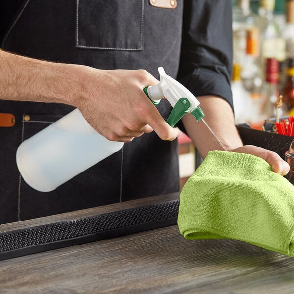 A person spraying a liquid onto a green towel on a counter.