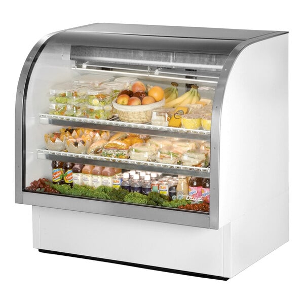 A True white curved glass refrigerated deli case full of food.