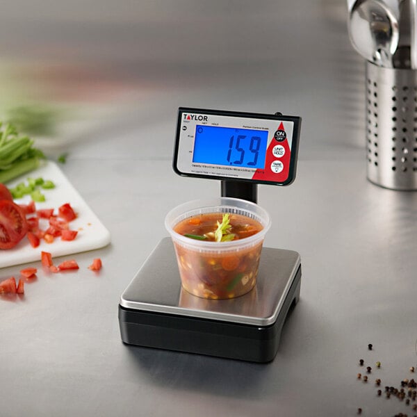 A Taylor digital portion scale with a cup of soup on it.
