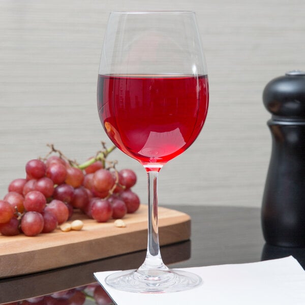 A Stolzle Weinland wine glass of red wine sits on a table next to grapes.