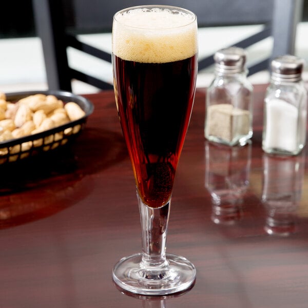 A Stolzle stemmed pilsner glass filled with beer on a table.
