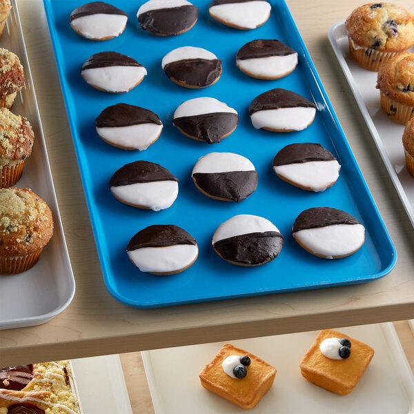 A blue Cambro market tray with pastries and muffins on a bakery display counter.