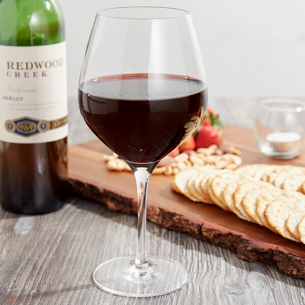 A Stolzle Exquisit burgundy wine glass of red wine next to a bottle of wine, crackers, and fruit.