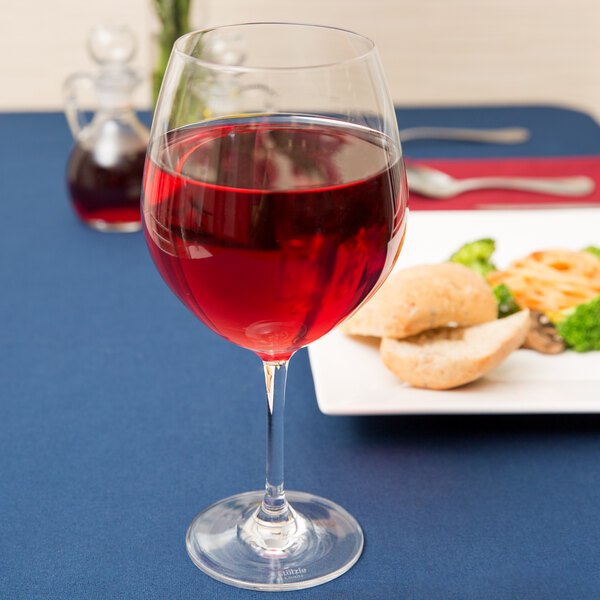 A Stolzle burgundy wine glass filled with red wine on a table in a fine dining restaurant.