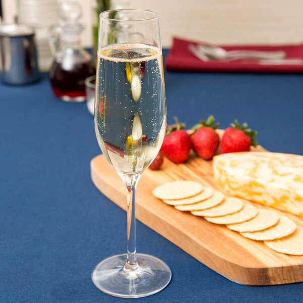 A Stolzle flute glass filled with champagne next to a cheese board with crackers and strawberries.