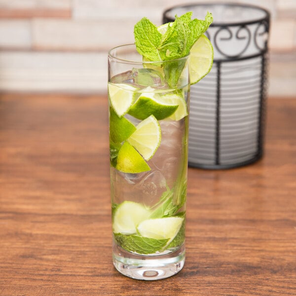 A Stolzle Collins glass of water with lime slices and mint leaves on a table in a cocktail bar.