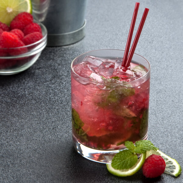 A Stolzle New York rocks glass filled with a red drink, straws, and lime slices on a table.