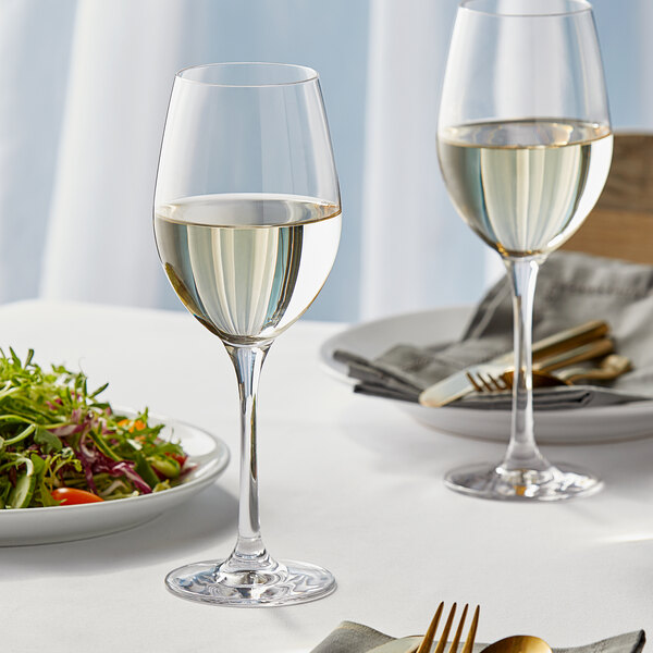 Two Stolzle New York Chardonnay wine glasses on a table with a plate of salad.