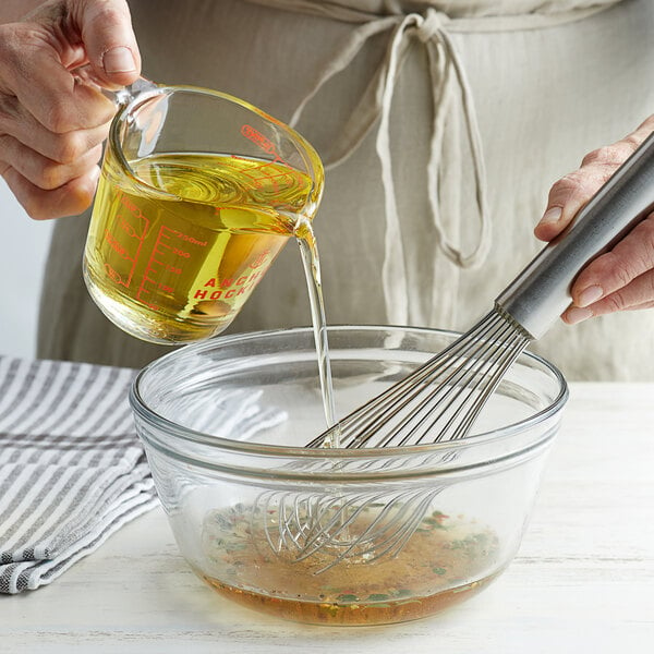 A person pouring 1 gallon corn oil into a bowl and using a whisk to mix it.