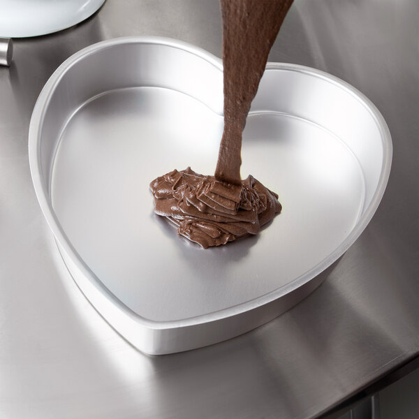 Liquid chocolate being poured into a Wilton heart-shaped cake pan.