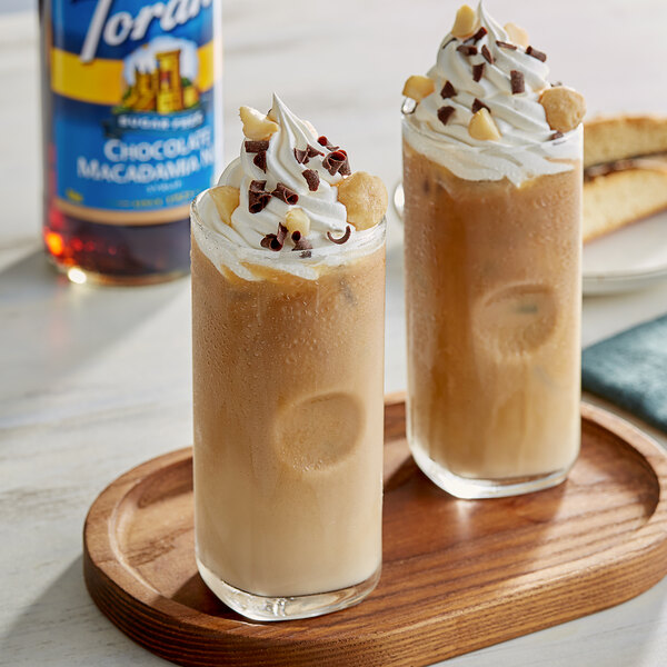 Two glasses of iced coffee with whipped cream and chocolate chips on a wooden tray.
