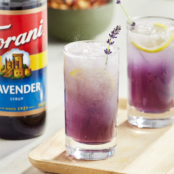 Two glasses of purple liquid with lemons and lavender flowers made with Torani Lavender Flavoring Syrup.