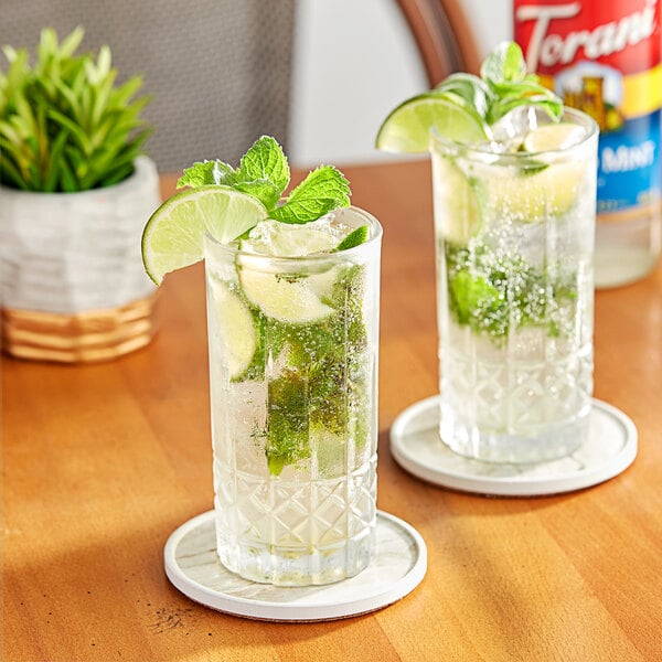 Two glasses of Torani Mojito with limes and mint on a table.