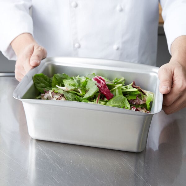 A chef holding a Vollrath stainless steel half size food pan filled with salad.