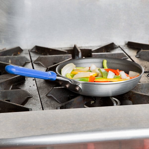 A Vollrath Wear-Ever aluminum non-stick fry pan filled with vegetables on a stove.