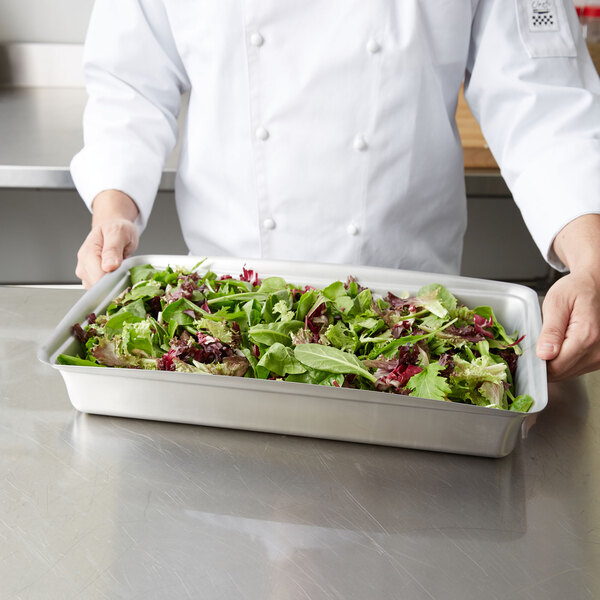 A chef holding a Vollrath stainless steel food pan filled with green and red lettuce.