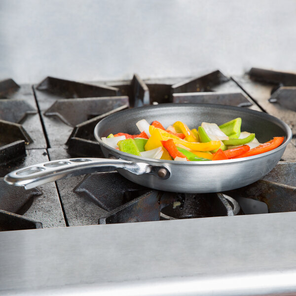 A Vollrath Wear-Ever aluminum non-stick fry pan with vegetables cooking in it on a stove.