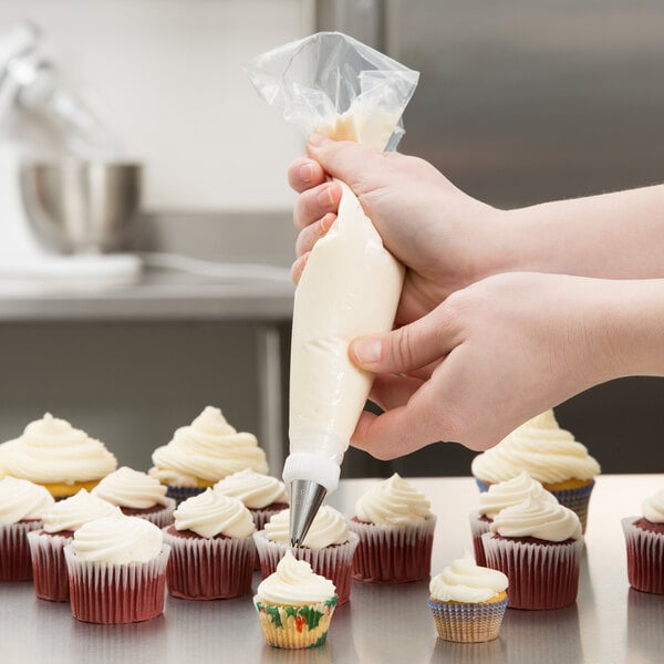 A person using an Ateco clear disposable pastry bag to frost cupcakes.