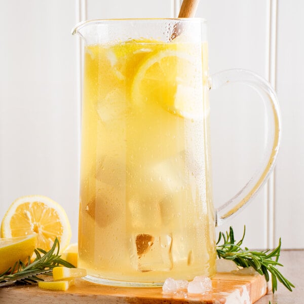 A glass pitcher of ReaLemon lemonade with ice cubes and lemons with a wooden spoon.