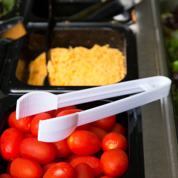 A tray of tomatoes with white plastic tongs.