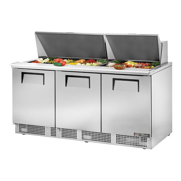 A stainless steel True refrigerated sandwich prep table with 3 doors and a food tray.