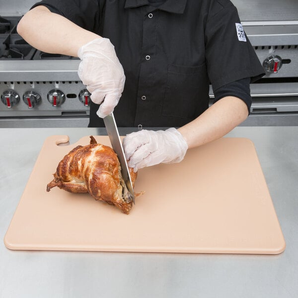 A person using a San Jamar color-coded cutting board to cut meat on a table.
