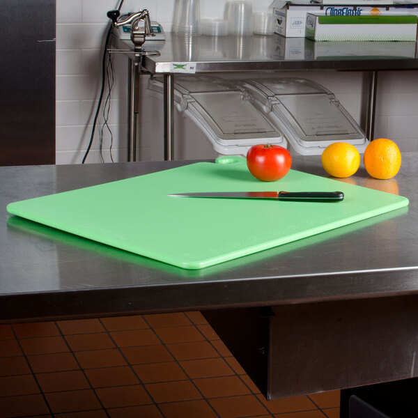 A San Jamar color-coded cutting board with a knife and oranges on a counter.