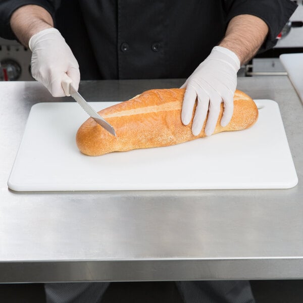 A person using a San Jamar color-coded cutting board to cut a loaf of bread.