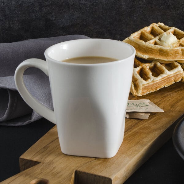 A white mug filled with a brown drink next to waffles with butter and a cup of coffee.