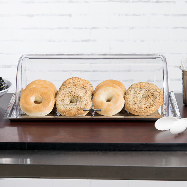 A Tablecraft rectangular polycarbonate roll top lid on a tray of bagels on a table.