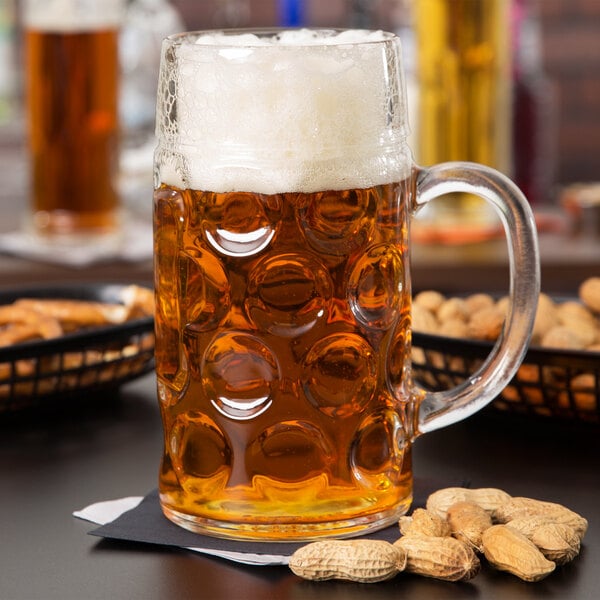 A Libbey Oktoberfest beer mug filled with beer and peanuts on a table.