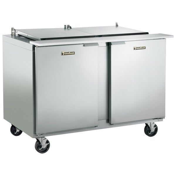 A stainless steel Traulsen refrigerated sandwich prep table with one left hinged door and one right hinged door on wheels.