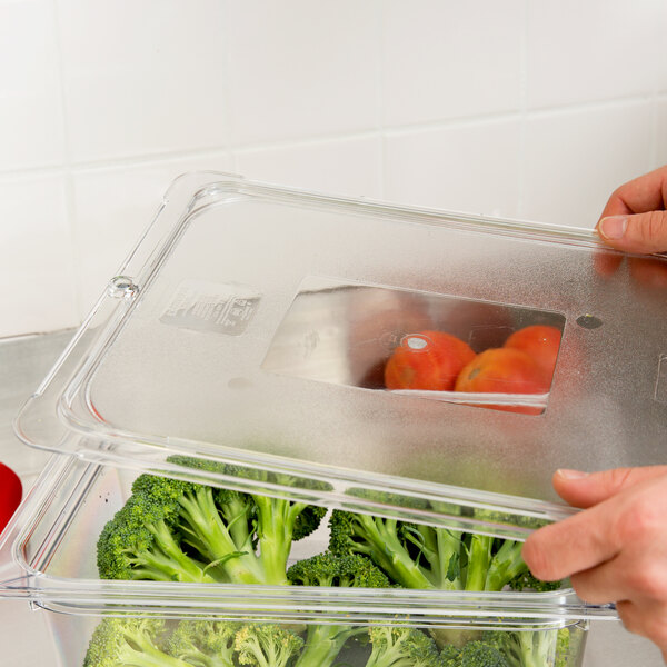 A person holding a Carlisle plastic container of broccoli with a clear plastic lid.