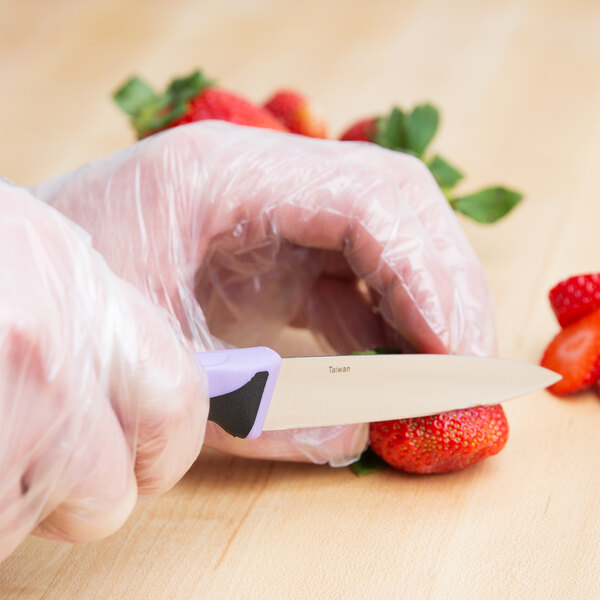 A person in plastic gloves using a Mercer Culinary purple paring knife to cut a strawberry.
