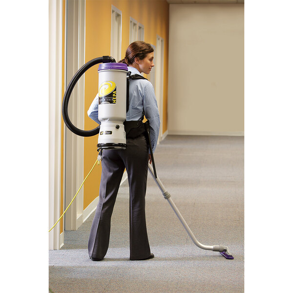 A woman using a ProTeam Super CoachVac backpack vacuum to clean the floor in a corporate office cafeteria.
