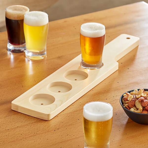 An Acopa natural wood flight paddle holding glasses of beer and nuts.
