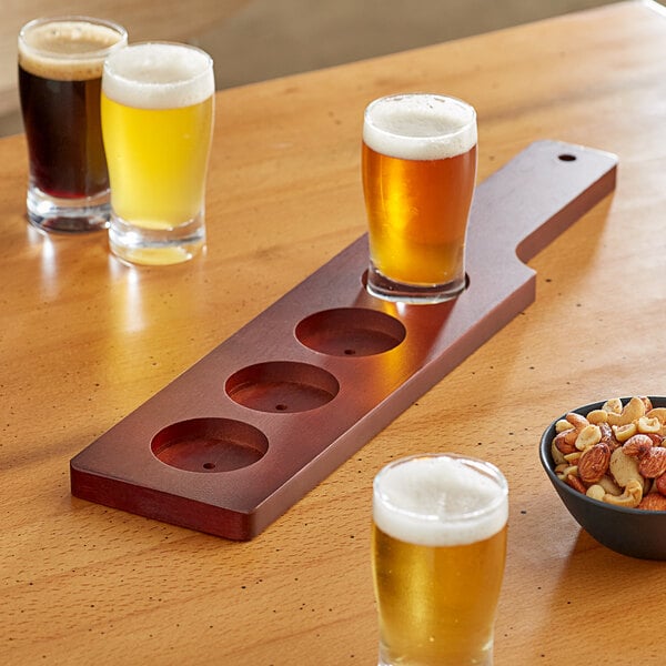 An Acopa mahogany beer flight paddle on a table with glasses of beer and a bowl of mixed nuts.
