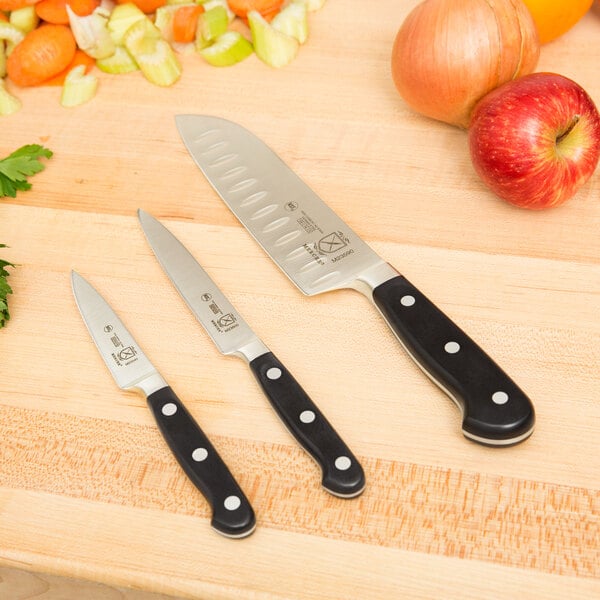 A Mercer Culinary Renaissance knife set on a wooden cutting board with a variety of fruits and vegetables.