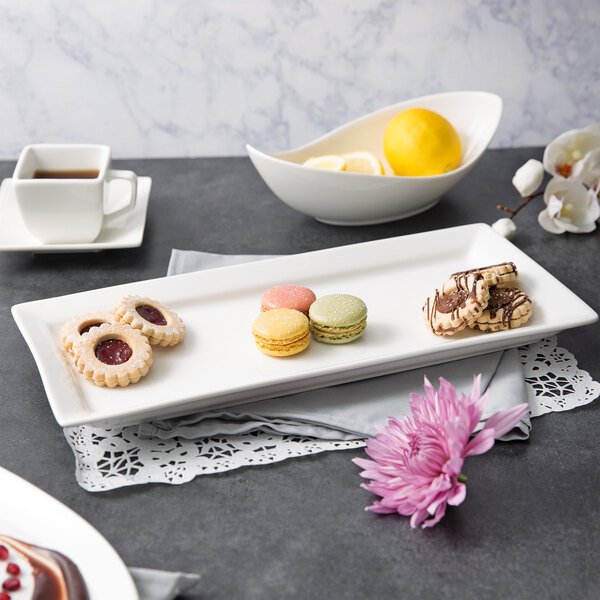 A white rectangular porcelain platter with cookies and fruit on a table.