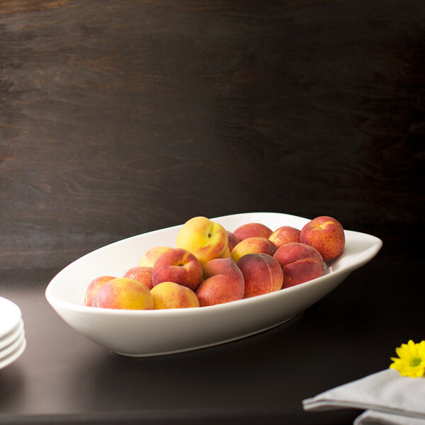 A 10 Strawberry Street Whittier white porcelain peach bowl filled with peaches on a table with a flower.
