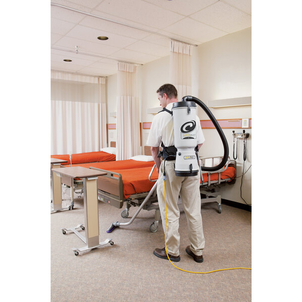 A man using a ProTeam LineVacer backpack vacuum to clean a hospital bed.