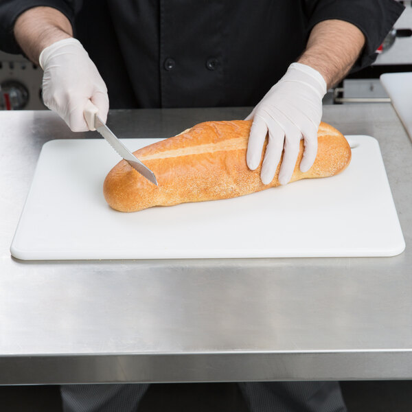 A person in a white glove cutting a loaf of bread on a San Jamar white cutting board.