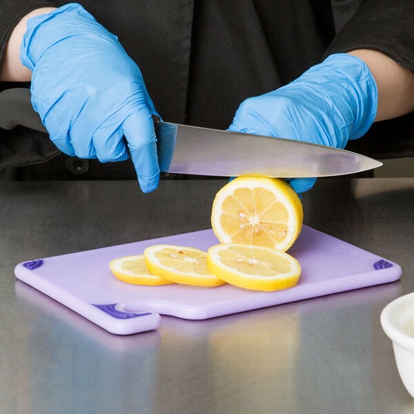 A person wearing blue gloves cutting lemons on a San Jamar purple allergen-free cutting board.