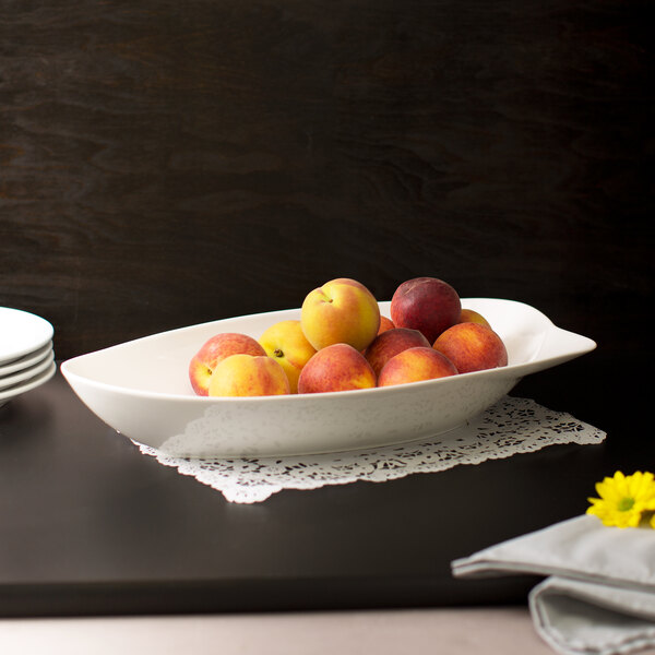 A white porcelain bowl filled with peaches on a table with a doily.