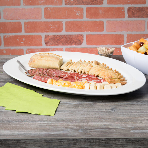 A white porcelain oval platter with a variety of meats and cheese on a table.