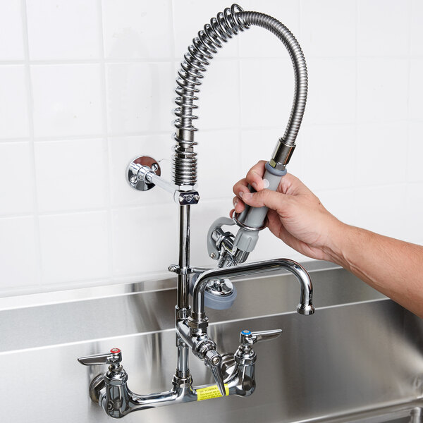 A person's hand holding a T&S wall mounted pre-rinse faucet with hose.
